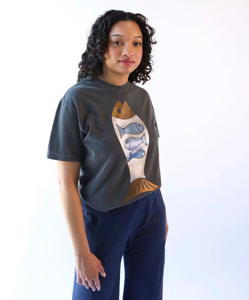 A woman wearing a dark gray cotton t-shirt with a foil fish design in bronze & blue