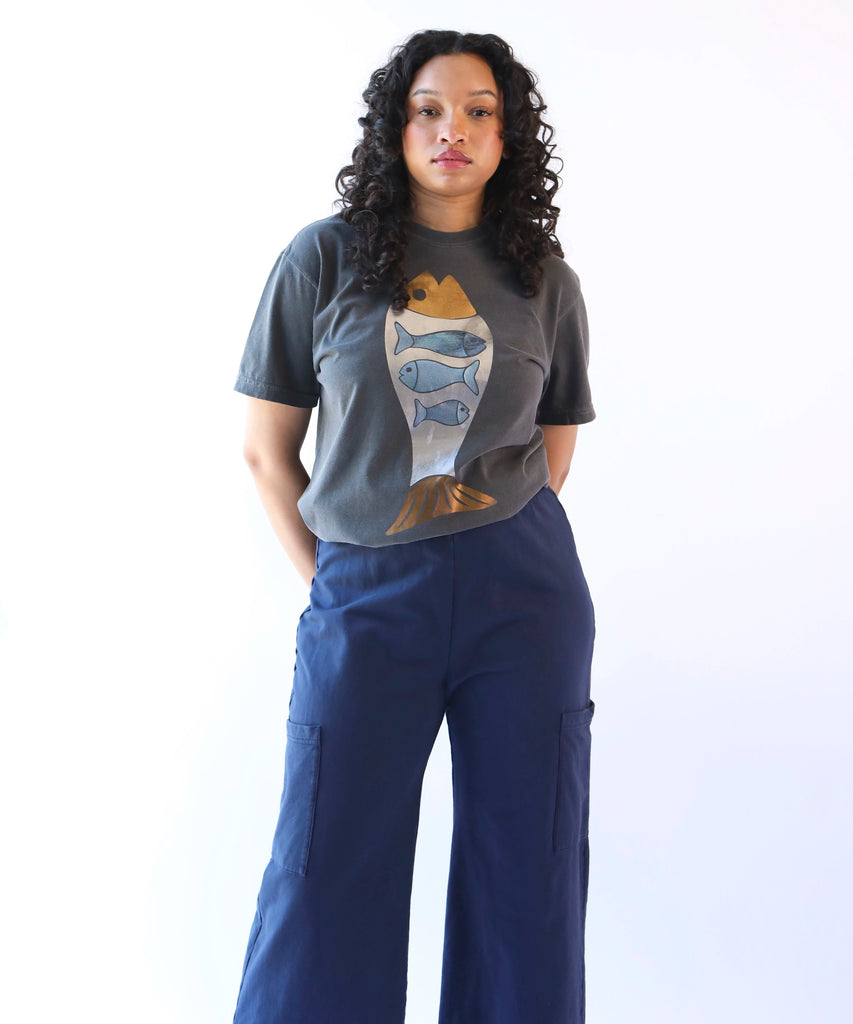 A woman wearing a dark gray cotton t-shirt with a foil fish design in bronze & blue with navy pants