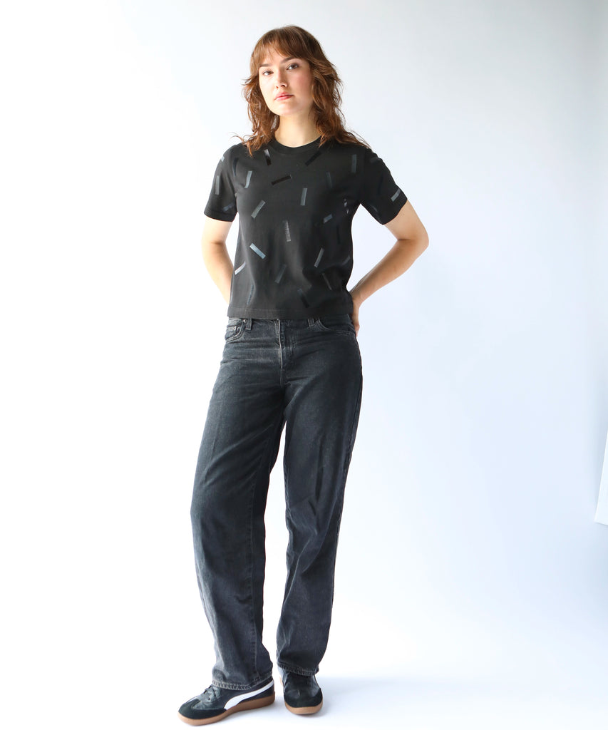 a woman wears a boxy cotton tshirt in black with black confetti sprinkle graphic print