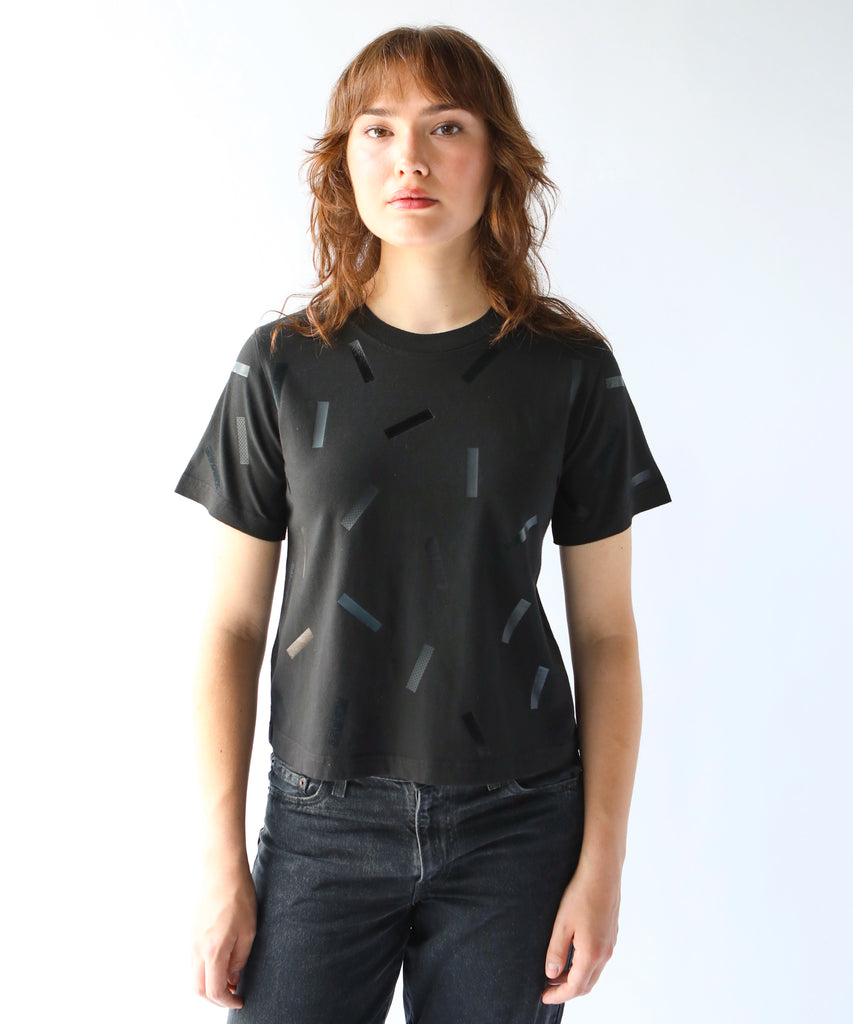 a woman wears a boxy cotton tshirt in black with black confetti sprinkle graphic print