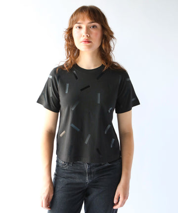 a woman wears a boxy cotton tshirt in black with black confetti sprinkle graphic print