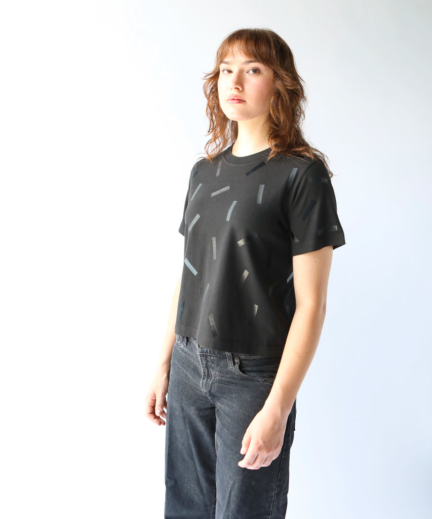 a woman wears a boxy cotton tshirt in black with black confetti sprinkle graphic print