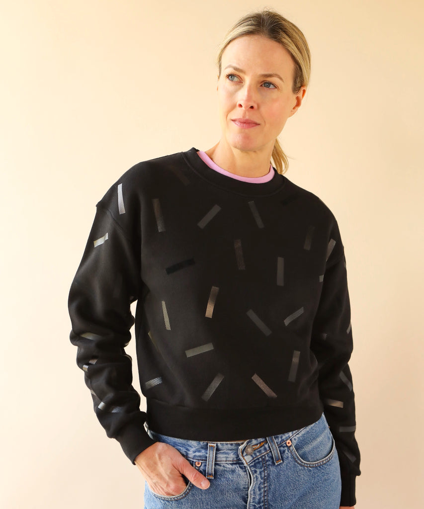 a woman wears a cotton sweatshirt in black with black confetti sprinkle graphic print