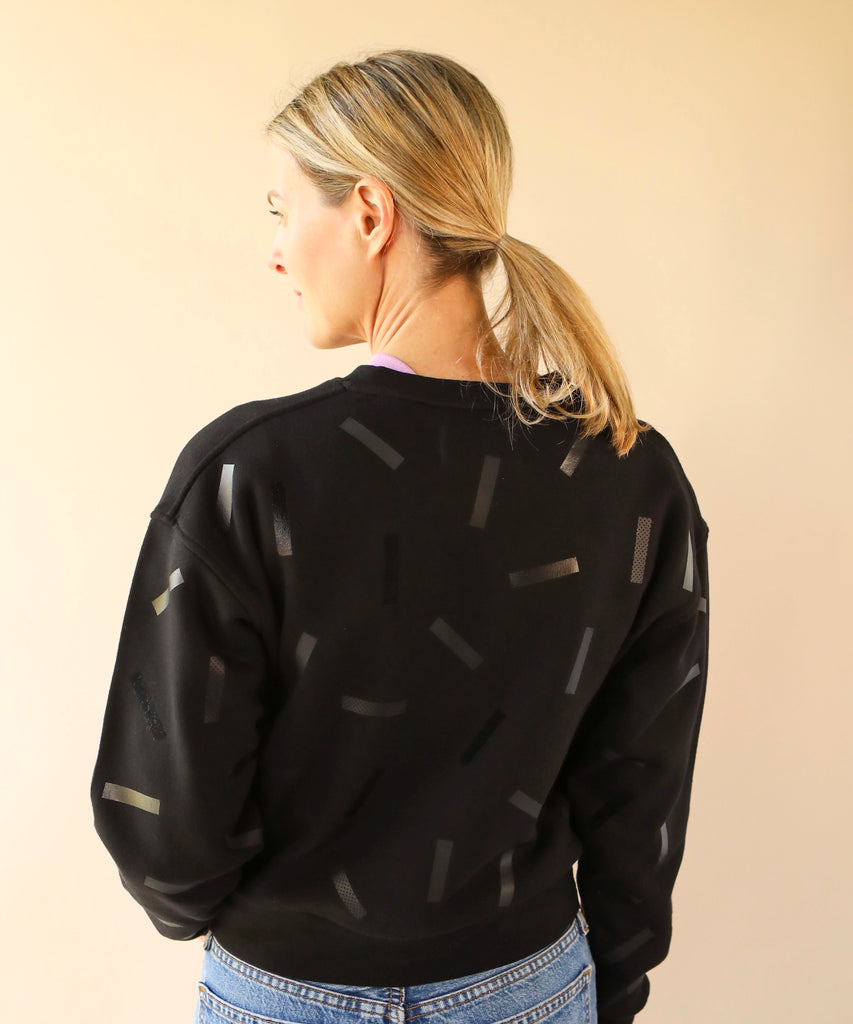a woman wears a cotton sweatshirt in black with black confetti sprinkle graphic print