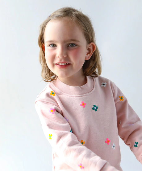 Young girl wearing a pink sweatshirt with colorful flower patterns on a white background