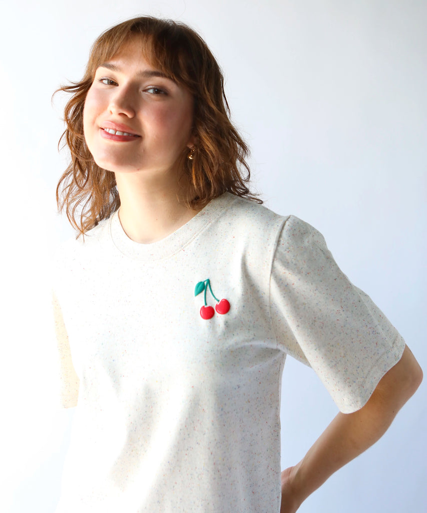 woman wearing a beige cotton tshirt with small cherry graphic over the left chest