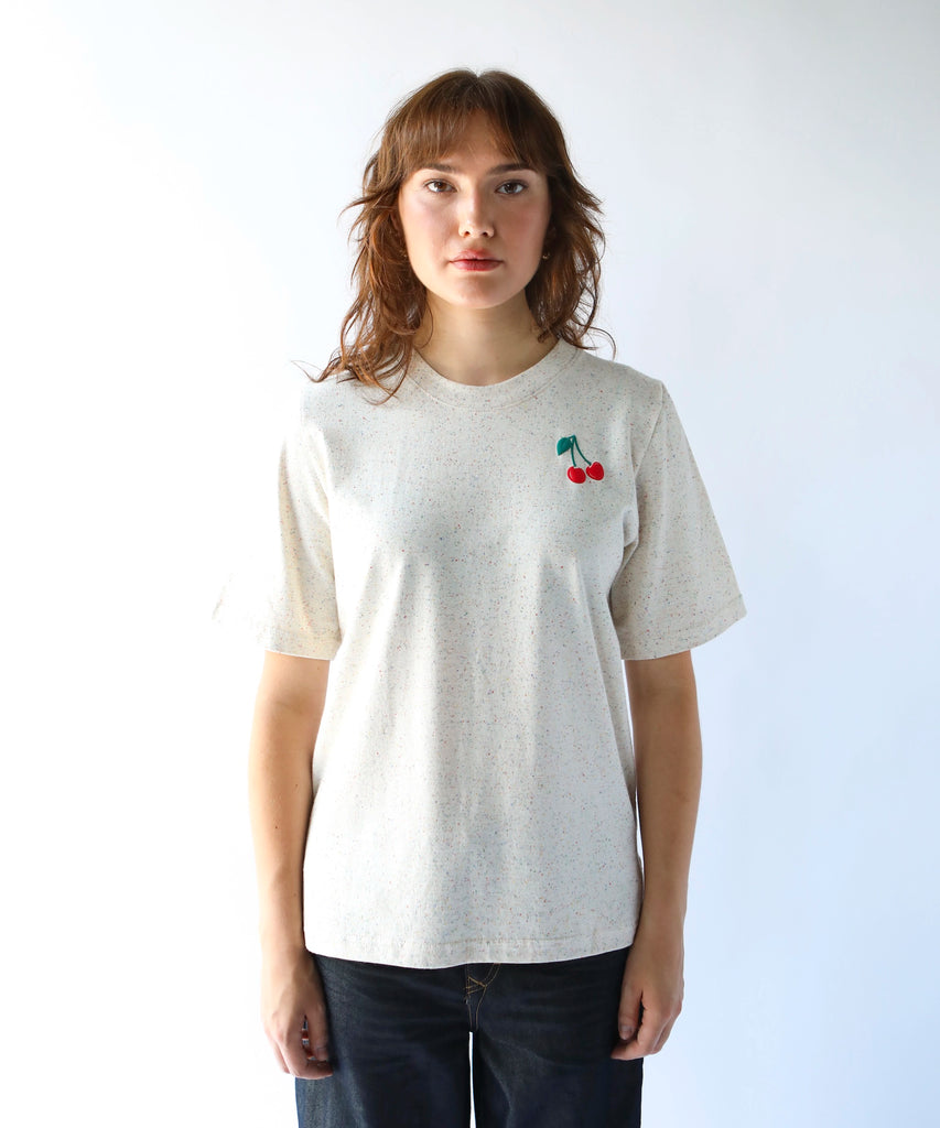 woman wearing a beige cotton tshirt with small cherry graphic over the left chest
