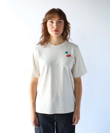 woman wearing a beige cotton tshirt with small cherry graphic over the left chest
