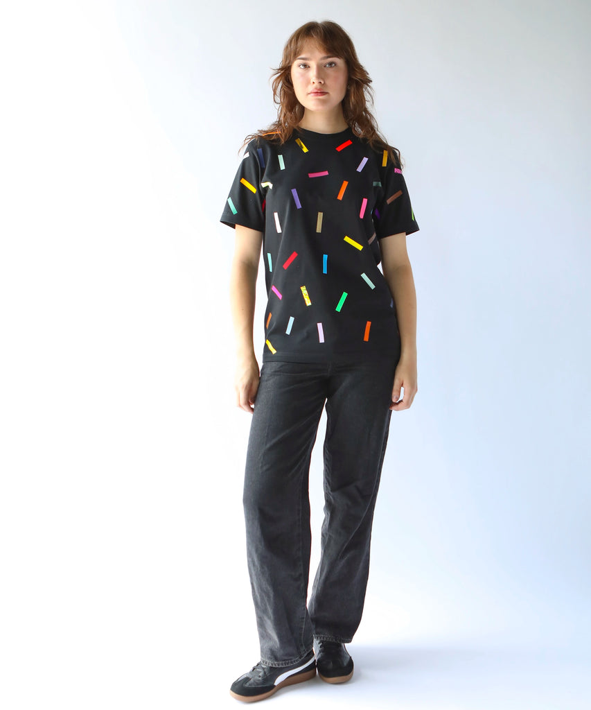 Woman wearing a black cotton t-shirt with colorful confetti sprinkles on it and black cotton pants