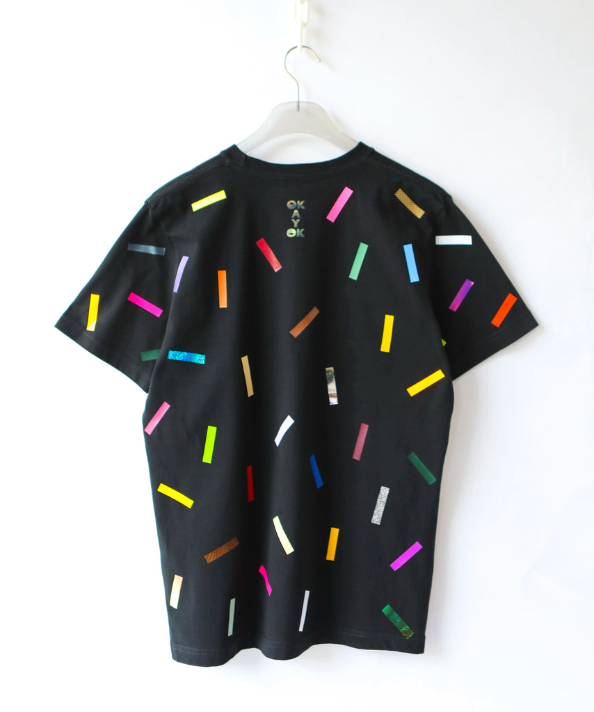 a black cotton t-shirt with colorful confetti sprinkles on it and a logo on the back saying 'OkayOk'