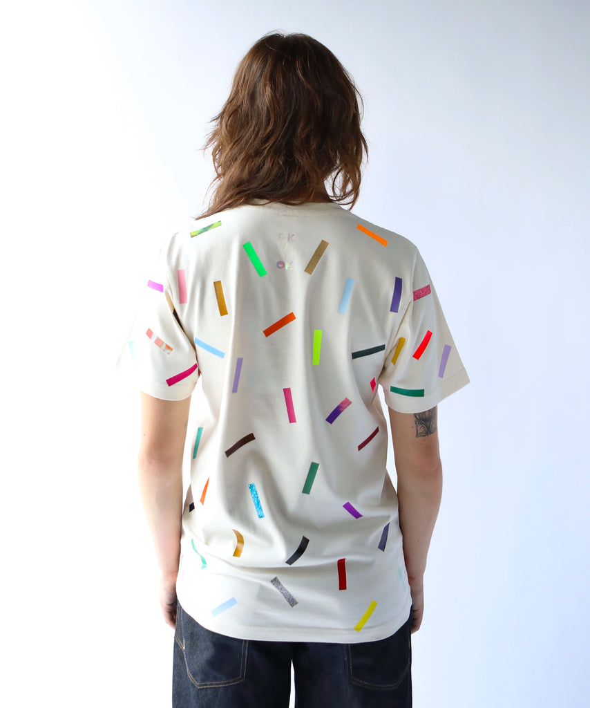 Woman wearing a cream cotton t-shirt with colorful confetti sprinkle pattern on it and 'okayok' logo