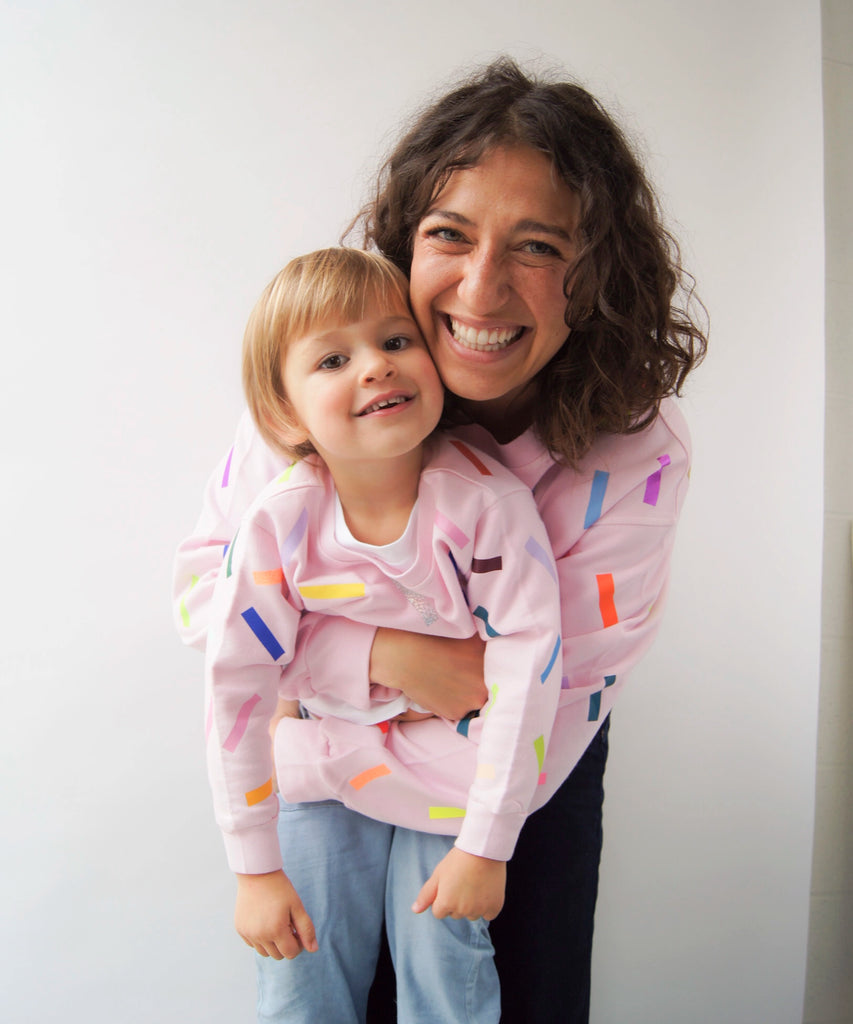 a woman and child each wear a cotton sweatshirt in pale pink with colourful confetti sprinkle graphic print