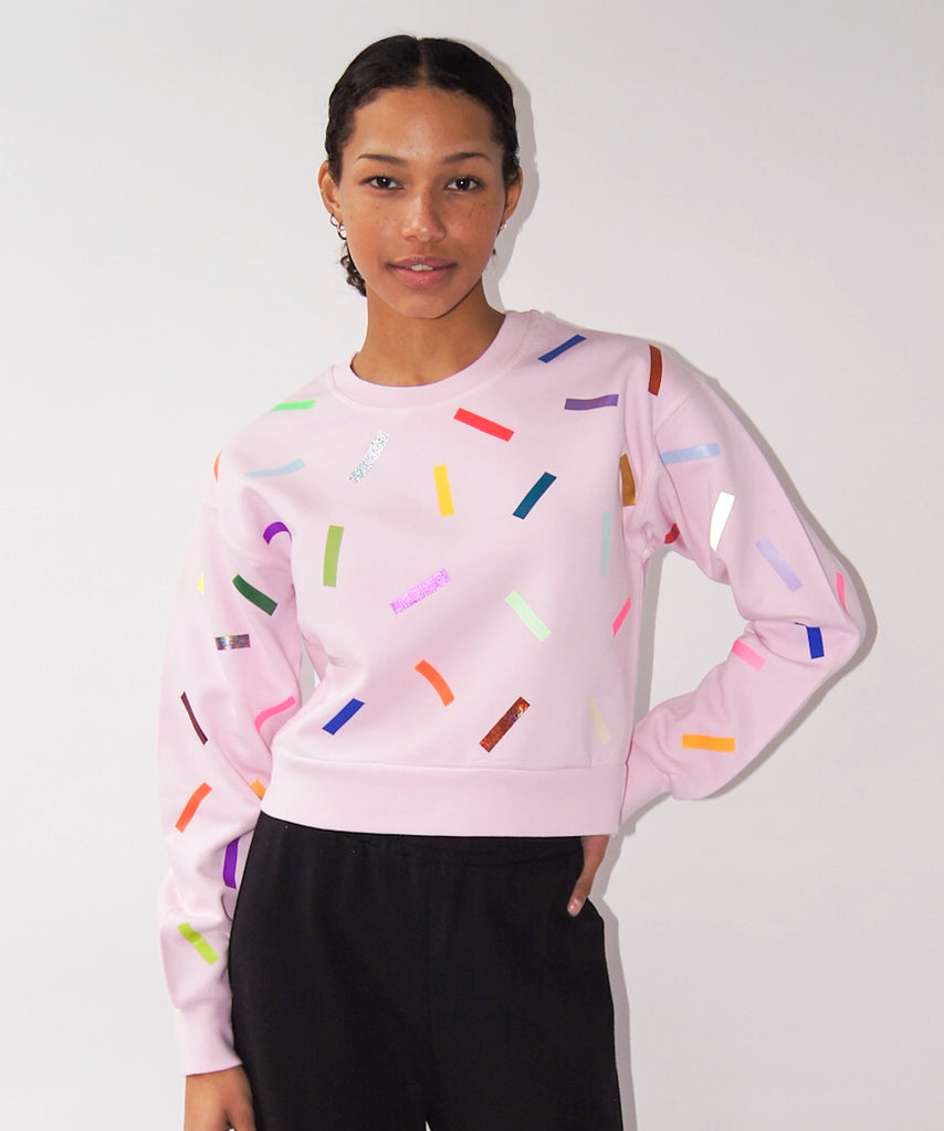 a woman wears a cotton sweatshirt in pale pink with colourful confetti sprinkle graphic print
