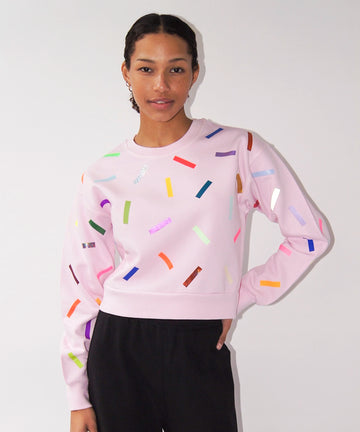 a woman wears a cotton sweatshirt in pale pink with colourful confetti sprinkle graphic print
