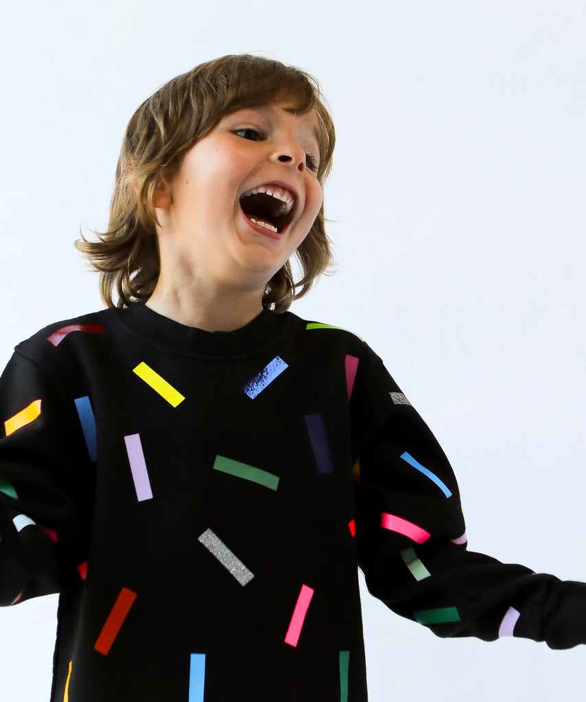 a kid wearing cotton sweatshirt in black with colourful confetti sprinkle pattern 