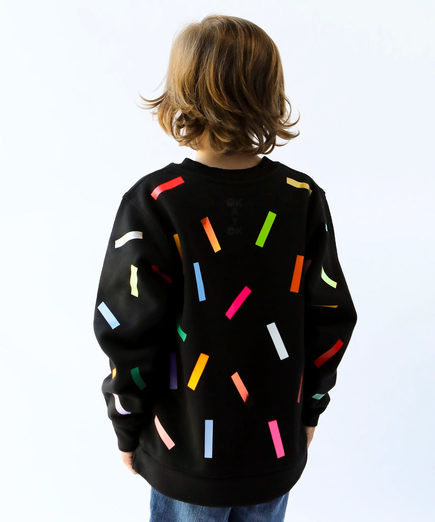 a kid wearing cotton sweatshirt in black with colourful confetti sprinkle pattern 