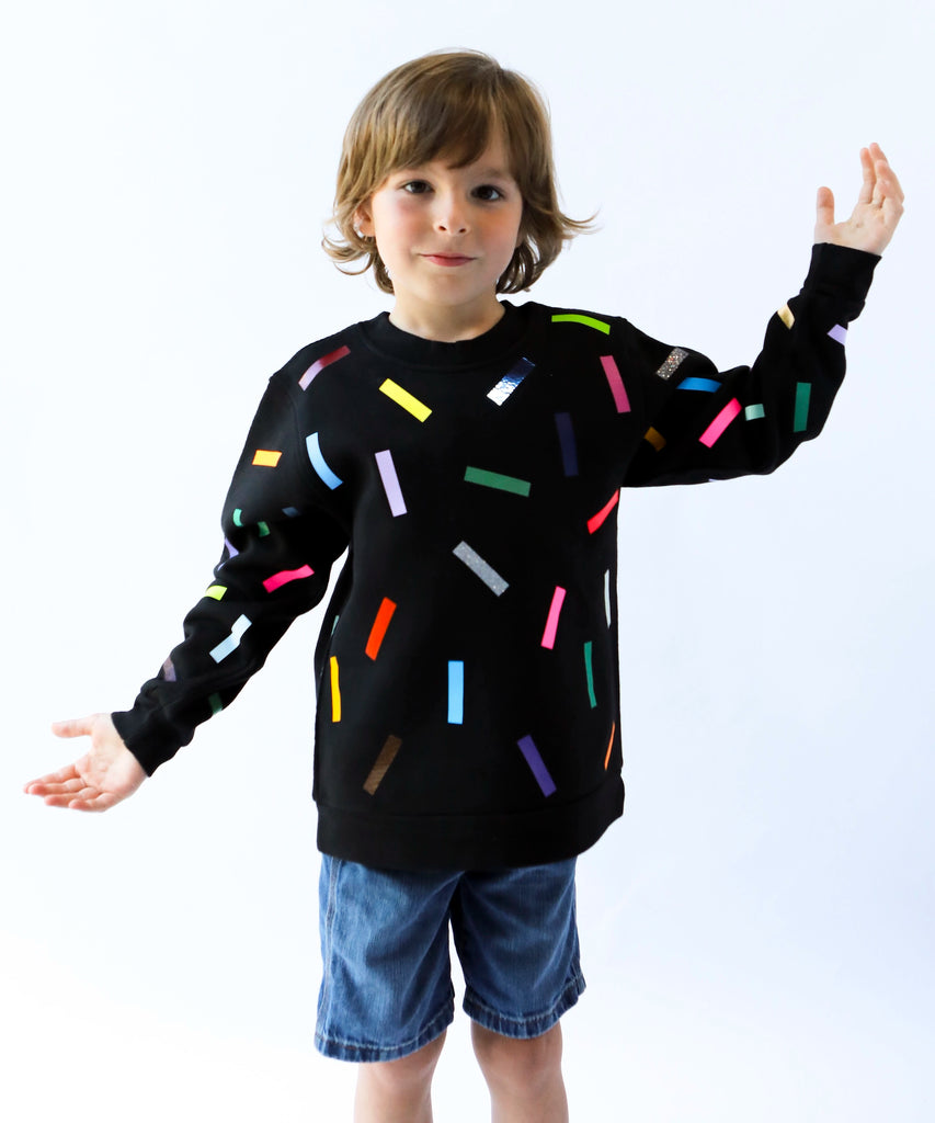 a kid wearing cotton sweatshirt in black with colourful confetti sprinkle pattern 
