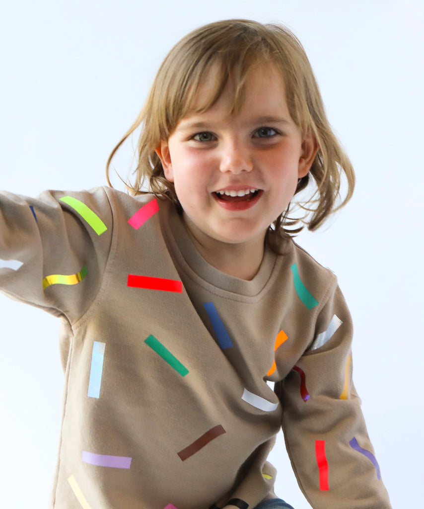 a kid wearing cotton sweatshirt in taupe beige with colourful confetti sprinkle pattern 