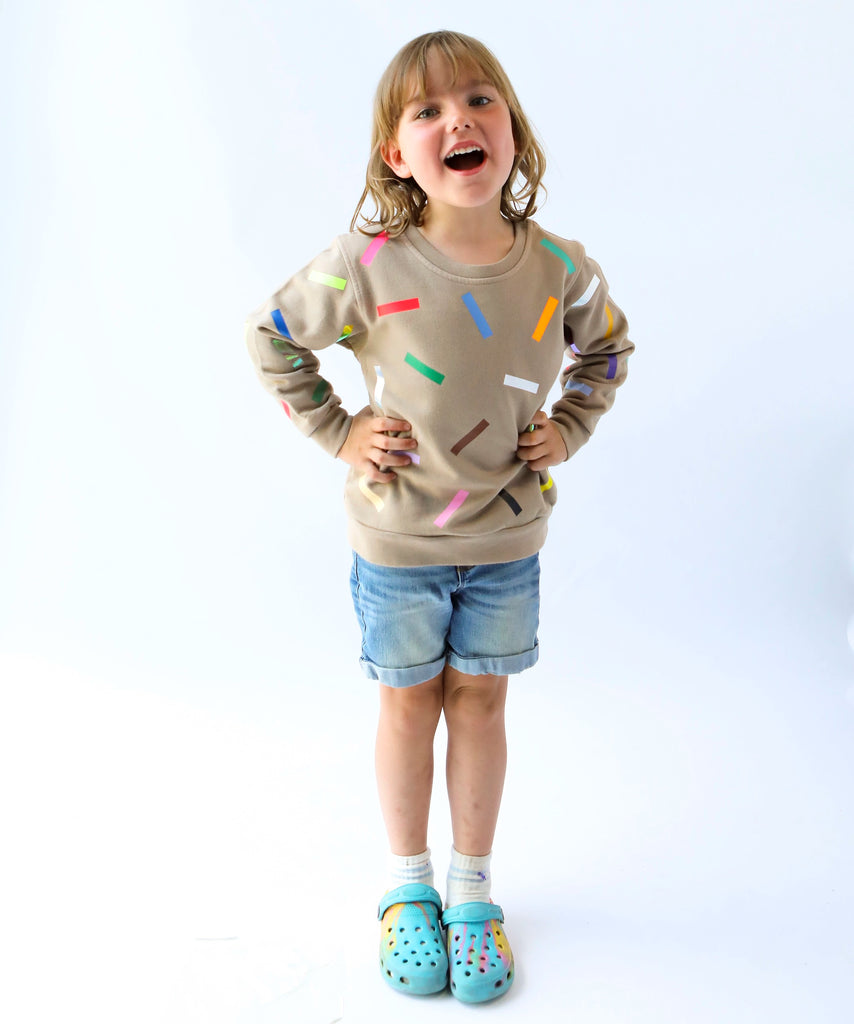 a kid wearing cotton sweatshirt in taupe beige with colourful confetti sprinkle pattern 