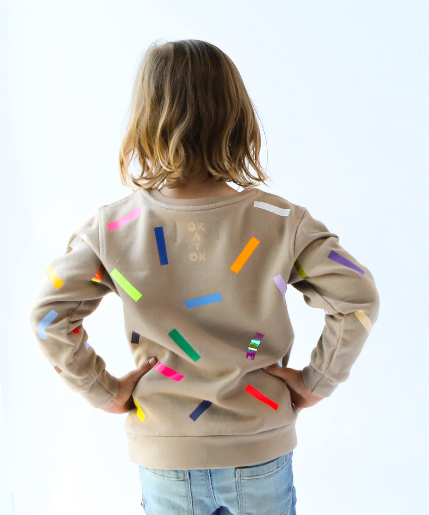 a kid wearing cotton sweatshirt in taupe beige with colourful confetti sprinkle pattern 