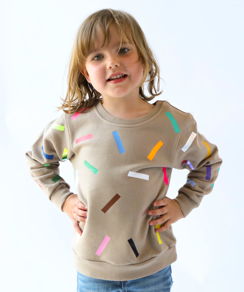 a kid wearing cotton sweatshirt in taupe beige with colourful confetti sprinkle pattern 