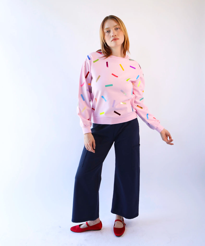 woman wearing a pink cotton sweatshirt with colorful sprinkles confetti pattern and black cotton pants