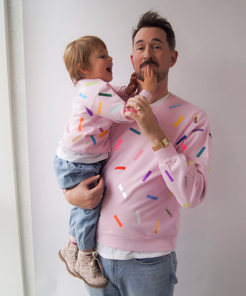 Man and child wearing matching pink sweatshirts with colorful sprinkles