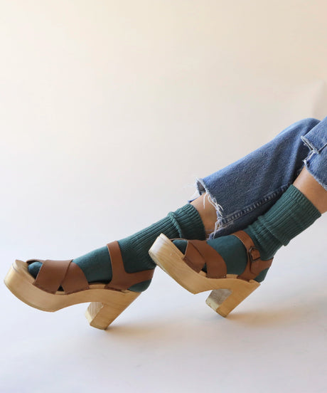A pair of unisex ribbed crew cotton socks in spruce green made in Canada by Toronto brand OkayOk styled with wooden clogs