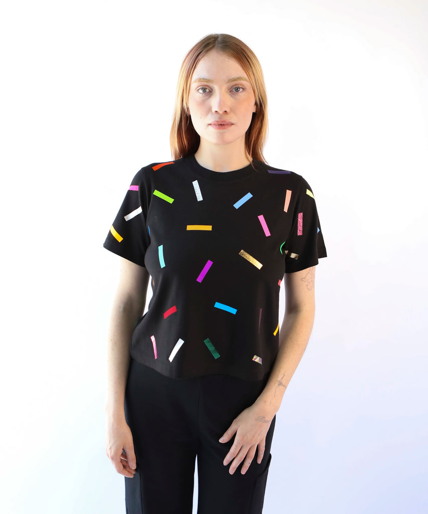 A woman wearing a cotton t-shirt with colorful confetti sprinkles pattern in black