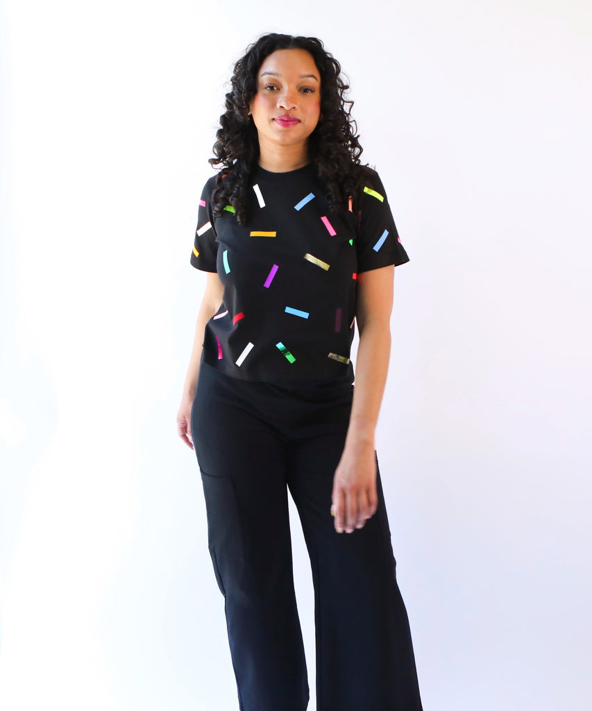 A woman wearing a cotton t-shirt with colorful confetti sprinkles pattern in black with black pants