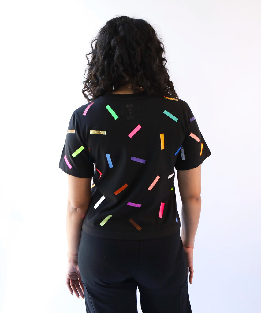 A woman wearing a cotton t-shirt with colorful confetti sprinkles pattern in black