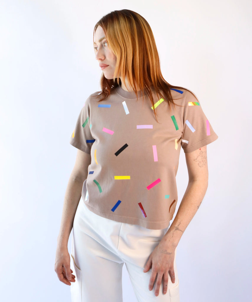 a woman wearing a taupe cotton t-shirt with colorful confetti sprinkles pattern in beige