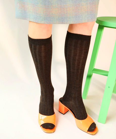 A person wears knee high wool socks in dark brown. Made in Canada by Toronto brand Okayok styled with orange patent heels