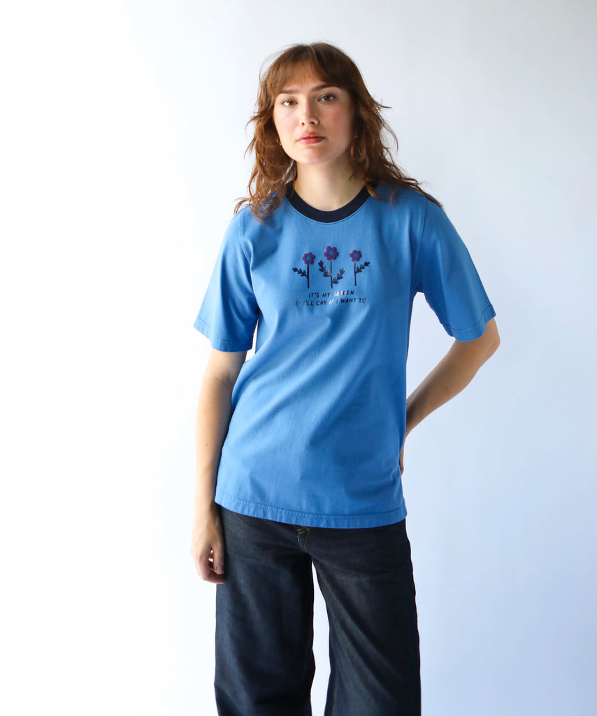 woman wearing a blue cotton graphic tshirt with flowers on it with a saying "It's my garden and I'll cry if I want to" and navy contrasting neckline