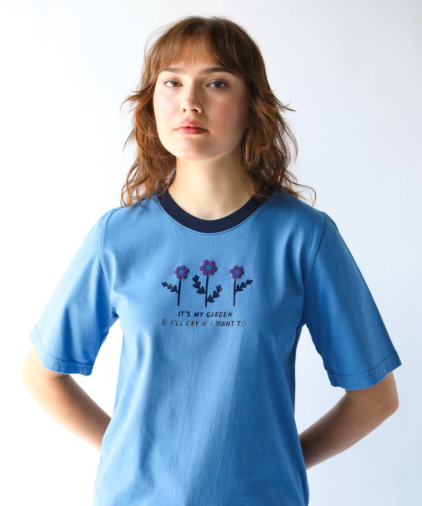 woman wearing a blue cotton graphic tshirt with flowers on it with a saying "It's my garden and I'll cry if I want to" and navy contrasting neckline