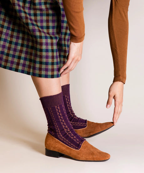 A pair of unisex, lightweight cable dressy cotton socks in plum made in Canada by Toronto brand OkayOk styled with plaid skirt and tan shoes