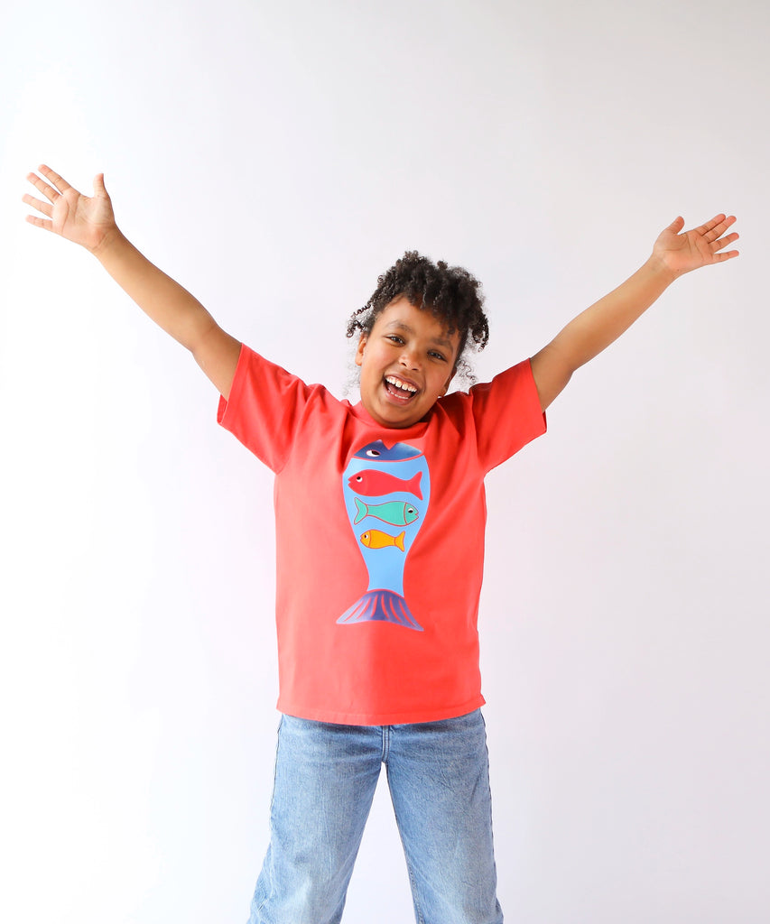 Child wearing a coral red cotton t-shirt with a colorful fish design 