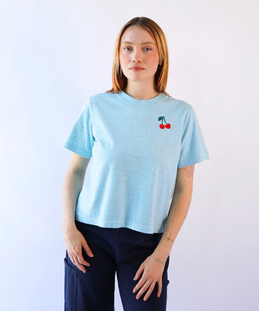 Person wearing a light blue cotton t-shirt with a cherry design on the top corner