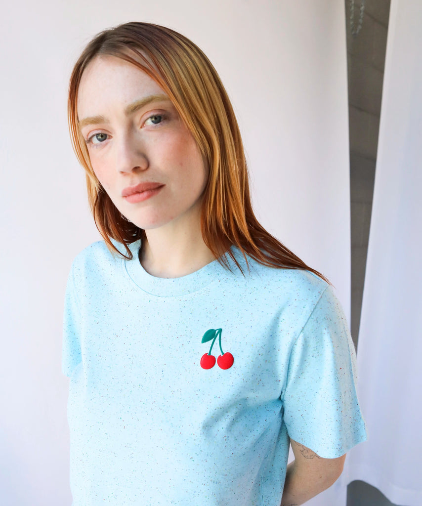Person wearing a light blue cotton t-shirt with a cherry design on the top corner
