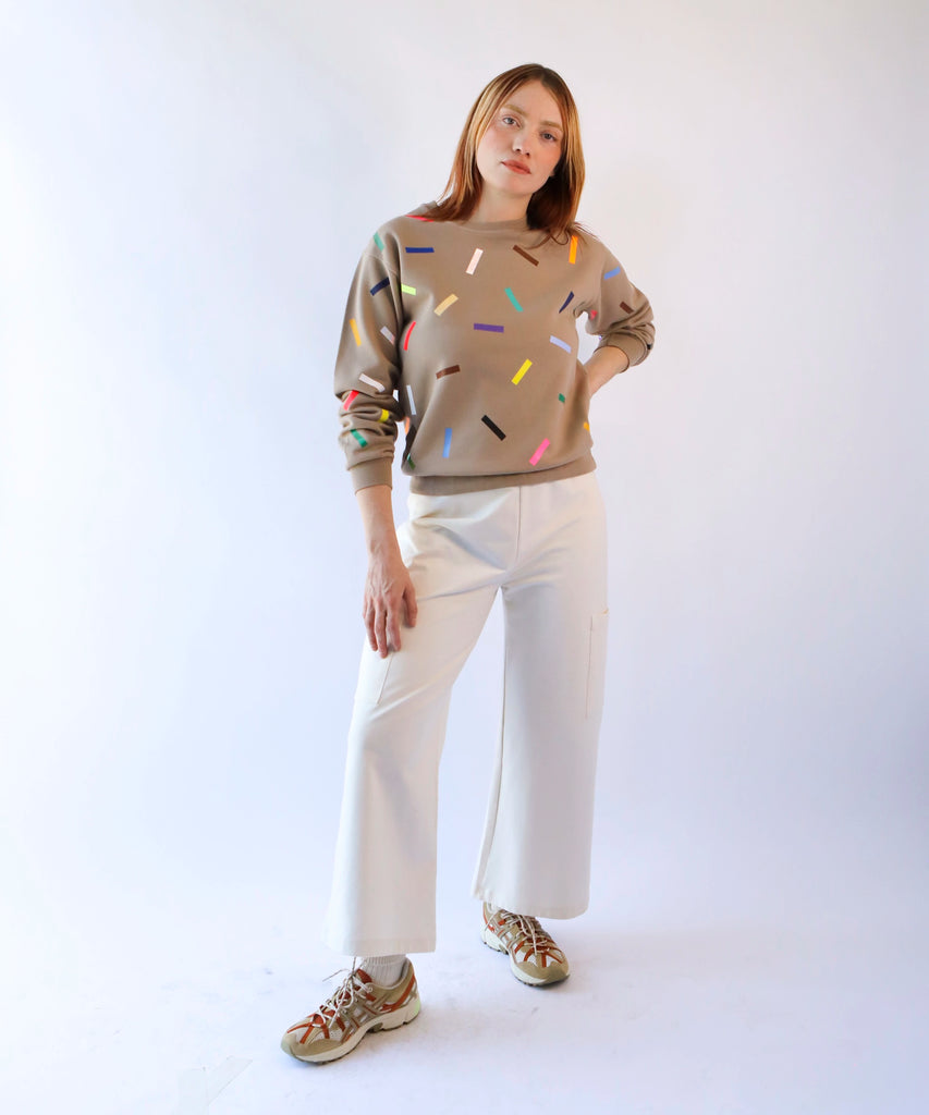 a woman wearing a taupe brown cotton sweatshirt with colorful sprinkles and white cotton pants