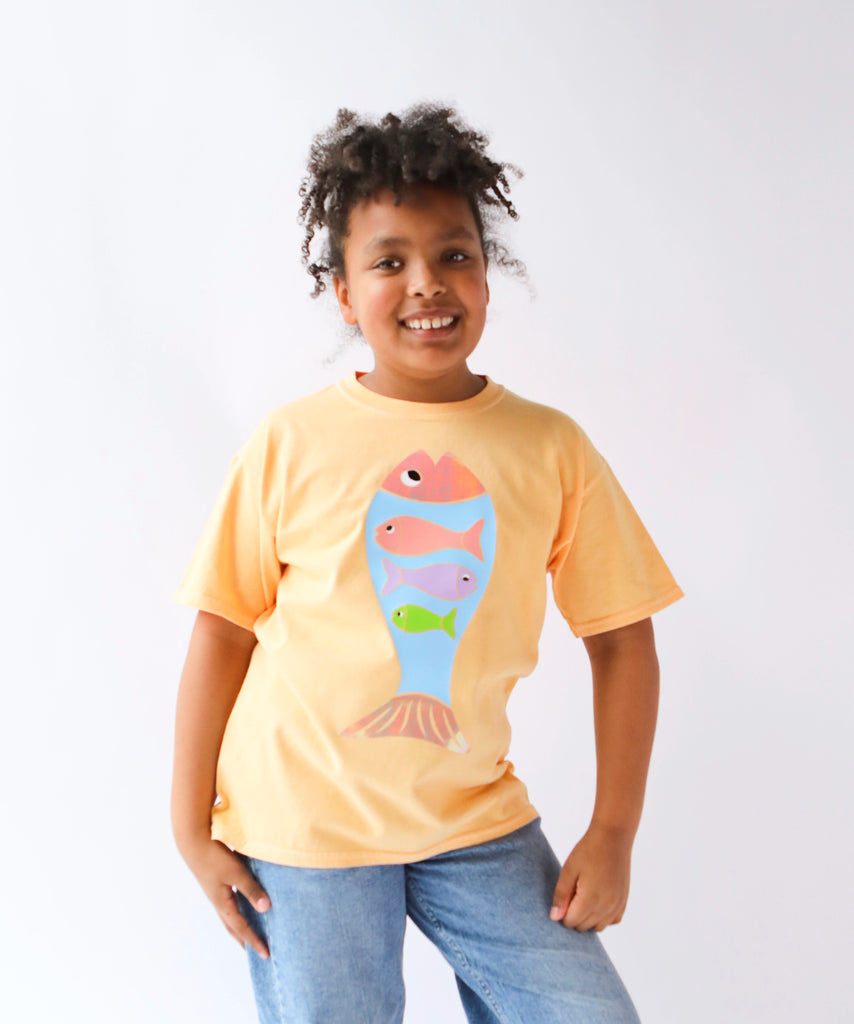 Child wearing a light orange cotton t-shirt with a colorful fish design in pastel colours