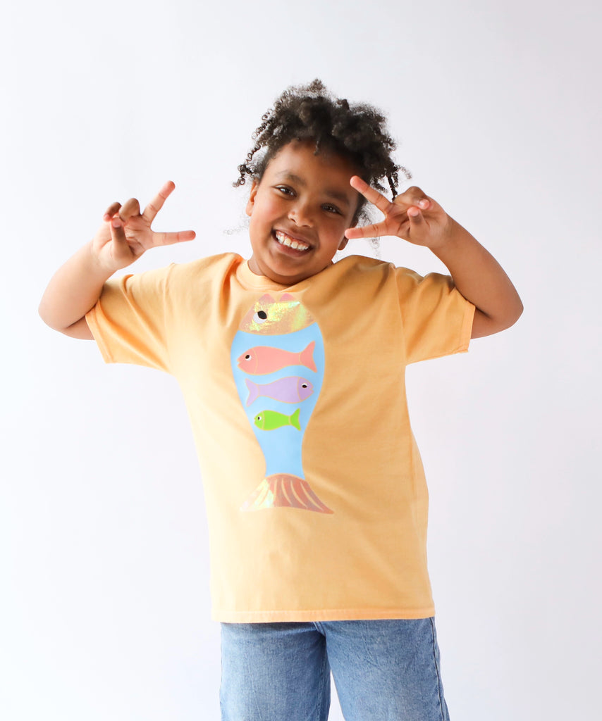 Child wearing a light orange cotton t-shirt with a colorful fish design in pastel colours
