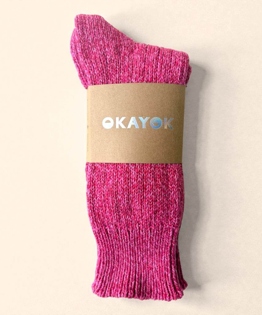 A pair of bright pink glittery knitted cotton socks with a brown label on a beige background. 