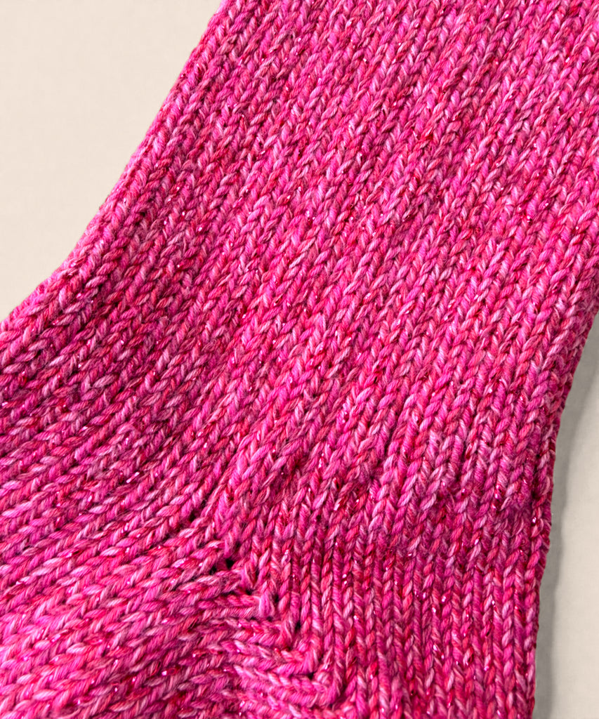 A close up of a pair of bright pink glittery knitted cotton socks on a beige background. 
