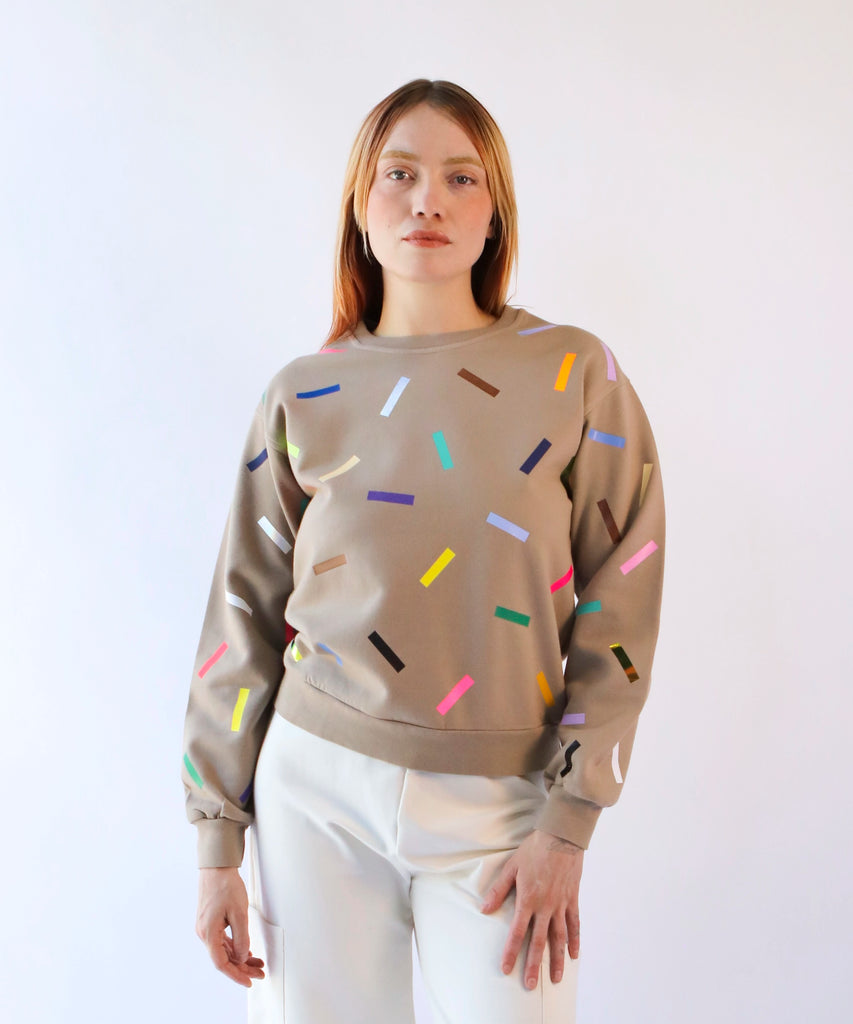 a woman wearing a beige cotton sweatshirt with colorful sprinkles 