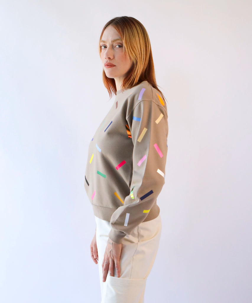 a woman wearing a beige cotton sweatshirt with a colorful sprinkles pattern