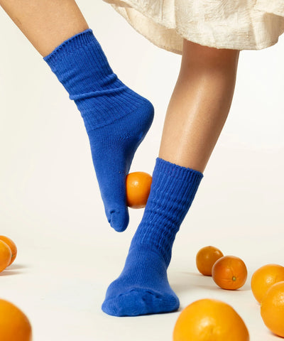 A pair of unisex ribbed crew cotton socks in cobalt blue made in Canada by Toronto brand OkayOk with clementines on the ground around them