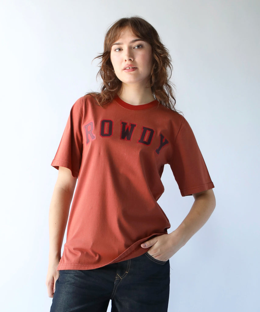 a woman wearing a cotton oversized tshirt with rowdy written in collegiate letters in rust colour