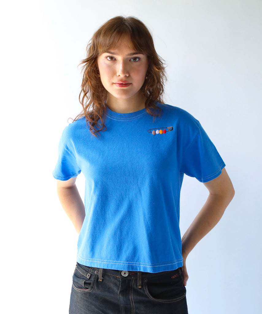Woman wearing a blue cotton t-shirt with a friendship pin graphic on it - safety pin with beads