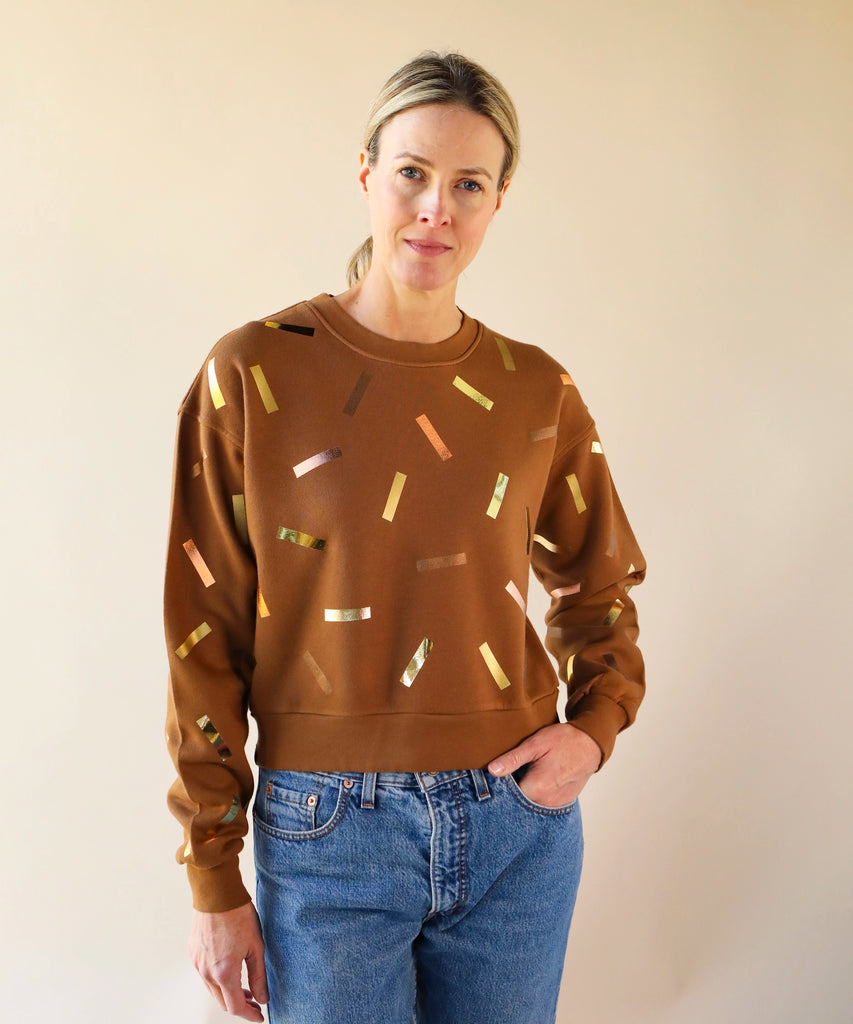 a woman wears a brown sweatshirt with gold and bronze confetti sprinkle print design
